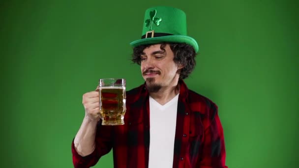 성 패트릭의 날. 젊은 옥 토버 페스트 남자가 녹색 배경에서 분리 된 음료와 함께 대형 맥주 머그를 나르고 있어. 느린 동작. — 비디오