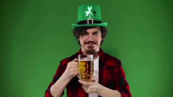 Dia de São Patrício. Homem Oktoberfest jovem servindo caneca de cerveja grande com bebida isolada em fundo verde. Movimento lento . — Vídeo de Stock