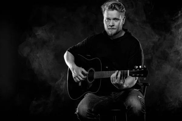 Handsome young musician man playing on guitar and singing in the smoke on stage or scene. — ストック写真