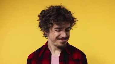 Handsome happy european man with curly hair shakes his head. Guy with beard and mustache in red shirt smiling and dancing isolated on yellow background. Lifestyle concept. Slow motion.