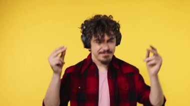 Handsome happy european man with beard in red shirt smiling and dancing isolated on yellow background. Guy in headphones listening to music. Lifestyle concept. Slow motion.
