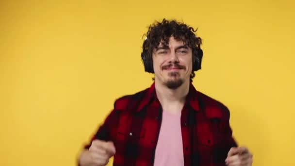 Guapo hombre europeo feliz con barba en camisa roja sonriendo y bailando aislado sobre fondo amarillo. Un tipo con auriculares escuchando música. Concepto de estilo de vida. Movimiento lento . — Vídeos de Stock