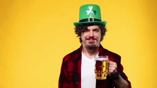 Saint Patrick Day. Young Oktoberfest man serving big beer mug with drink isolated on yellow background. Guy showing thumbs up sign with fingers. — Stock Video