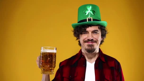 Saint Patrick Day. Young Oktoberfest man serving big beer mug with drink isolated on yellow background. Slow Motion. — Stock Video