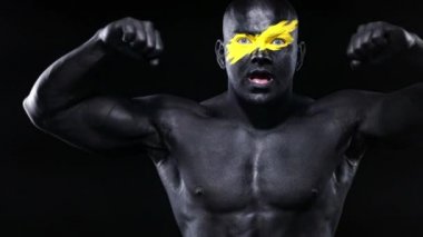 Yüz sanatında sarı renkli ve siyah vücut boyalı erkek vücut geliştirme sporcusu kasları çalıştırıyor. Bodyart 'lı adamın renkli portresi.