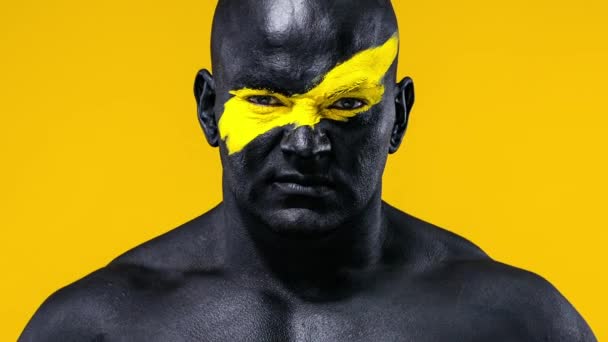 Man sports fan celebrates team victory. Bodybuilder athlete with yellow color on face art and black body paint. Colorful portrait of the guy with bodyart. — Stock Video