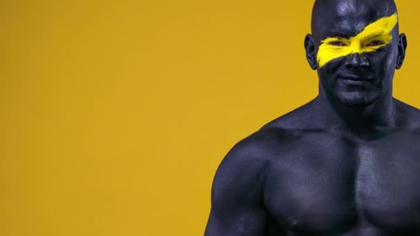 Homme fan de sport et athlète bodybuilder avec la couleur jaune sur le visage et la peinture du corps noir. Portrait coloré du gars avec bodyart. Le gars montrant les pouces vers le haut signe avec les doigts . — Video