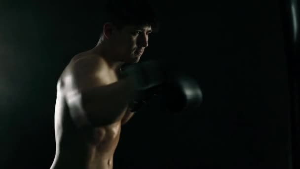Boxkonzept. Boxermann in Handschuhen kämpft mit Boxsack auf schwarzem Hintergrund. Individuelle sportliche Erholung. Zeitlupe. — Stockvideo