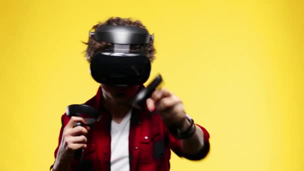 Young man with curly hair using a VR headset and experiencing virtual reality isolated on yellow background — Stockvideo