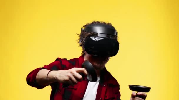 Молодий чоловік з кучерявим волоссям використовує гарнітуру VR і відчуває віртуальну реальність ізольовано на жовтому фоні — стокове відео