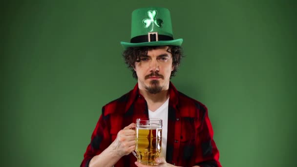 Saint Patrick. Jeune homme Oktoberfest servant une grande tasse de bière avec une boisson isolée sur fond vert. Mouvement lent . — Video