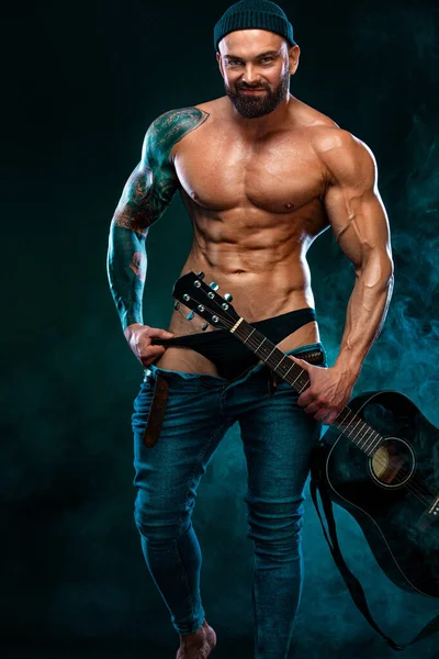 Сильный и здоровый бодибилдер с гитарой показывает мышцы живота. Спортивный мускулистый спортсмен. Концепция спорта и фитнеса. Мужская мода . — стоковое фото