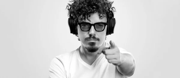 Retrato de hombre barbudo feliz con el pelo rizado apuntando con el dedo a la pantalla aislado sobre fondo amarillo. Chico en gafas de sol azules y auriculares escogen gran idea . — Foto de Stock