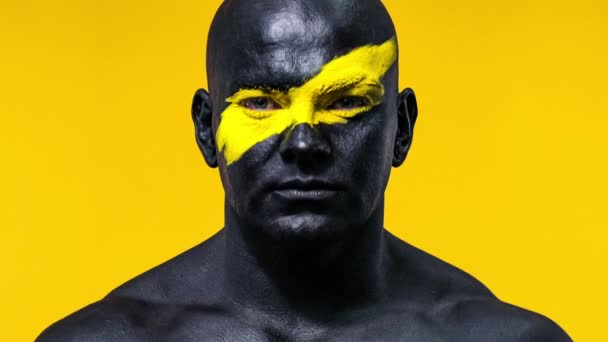 Чоловік бодібілдер з жовтим кольором на обличчі мистецтва і чорна фарба для тіла. Барвистий портрет хлопця з бодіарт . — стокове відео