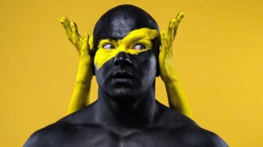 Vücudunda kadın eli olan bir adam. Sarı yüzlü ve siyah vücut boyalı vücut geliştirme sporcusu. Bodyart 'lı adamın renkli portresi.