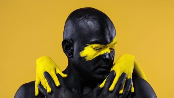 Homme avec des mains féminines sur le corps. Athlète bodybuilder avec l'art du visage jaune et la peinture de corps noire. Portrait coloré du gars avec bodyart . — Video