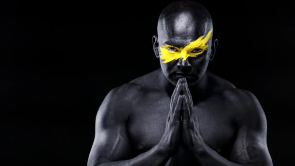 Man sports fan and bodybuilder athlete with yellow color on face art and black body paint. Colorful portrait of the guy with bodyart. Guy showing namaste sign with hands. — Stock Video