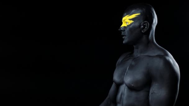 Een man pikt kopieerruimte in. Bodybuilder atleet met gele gezicht kunst en zwarte body paint. Kleurrijk portret van de man met bodyart. — Stockvideo