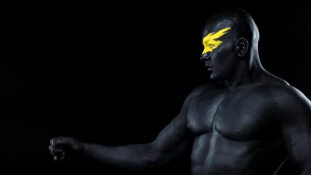 Een man pikt kopieerruimte in. Bodybuilder atleet met gele gezicht kunst en zwarte body paint. Kleurrijk portret van de man met bodyart. — Stockvideo