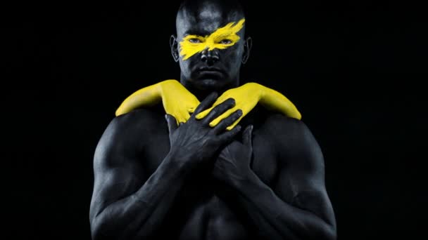 Man with female hands on the body. Bodybuilder athlete with yellow face art and black body paint. Colorful portrait of the guy with bodyart. — Stock Video