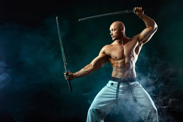 Karate fighter on black background with smoke. Shirtless man samurai with Japanese sword. Fit man sportsmen bodybuilder physique and athlete. Mens sport motivation.