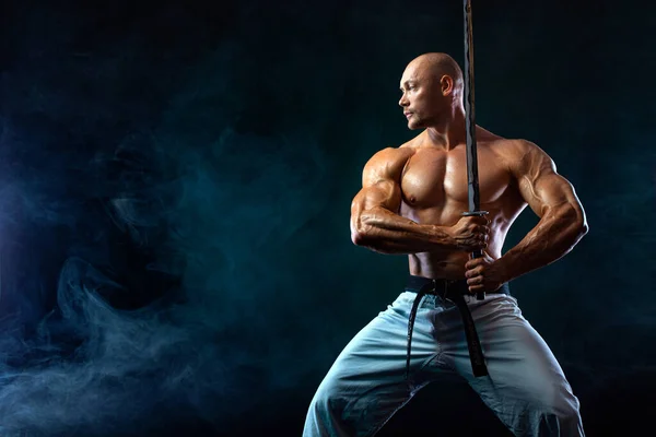 Karate bojovník na černém pozadí s kouřem. Samuraj bez košile s japonským mečem. Fit man sportovci kulturista postava a sportovec. Sportovní motivace mužů. — Stock fotografie