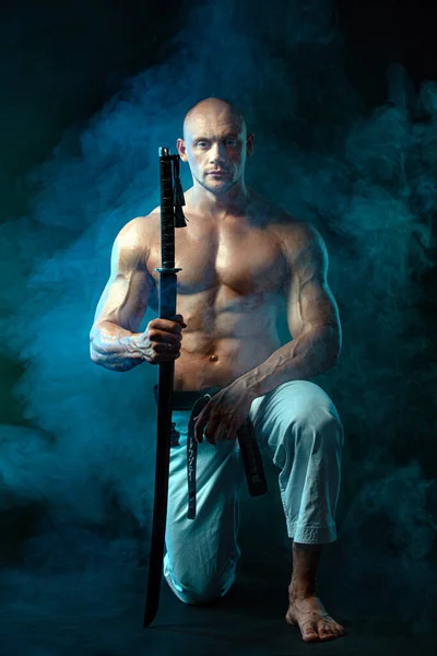 Karate harcos fekete háttérrel, füsttel. Félmeztelen szamuráj japán karddal. Alkalmas férfi sportolók testépítő fizikum és sportoló. Férfi sport motiváció. — Stock Fotó