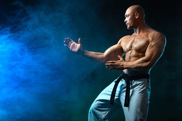 Caça de karatê ou taekwondo sobre fundo preto com fumaça. Apto homem desportistas fisiculturista físico e atleta. Motivação desportiva masculina . — Fotografia de Stock