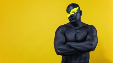 Erkek spor hayranı ve vücut geliştirme sporcusu. Yüz ve vücut boyalarında sarı renkli. Bodyart 'lı adamın renkli portresi. Adam parmaklarıyla işaret veriyor. Yavaş çekim.