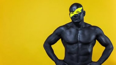 Erkek spor hayranı ve vücut geliştirme sporcusu. Yüz ve vücut boyalarında sarı renkli. Bodyart 'lı adamın renkli portresi. Adam parmaklarıyla işaret veriyor. Yavaş çekim.