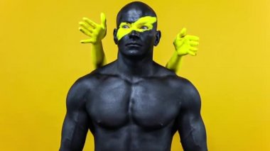 Vücudunda kadın eli olan bir adam. Sarı yüzlü ve siyah vücut boyalı vücut geliştirme sporcusu. Bodyart 'lı adamın renkli portresi. Yavaş çekim.