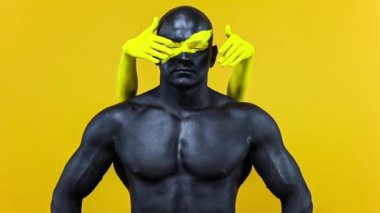 Vücudunda kadın eli olan bir adam. Sarı yüzlü ve siyah vücut boyalı vücut geliştirme sporcusu. Bodyart 'lı adamın renkli portresi. Yavaş çekim.