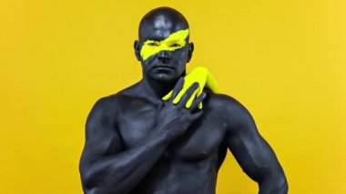 Vücudunda kadın eli olan bir adam. Sarı yüzlü ve siyah vücut boyalı vücut geliştirme sporcusu. Bodyart 'lı adamın renkli portresi. Yavaş çekim.