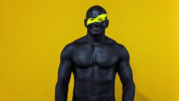 Uomo bodybuilder atleta con colore giallo sulla faccia arte e vernice corpo nero. Ritratto colorato del ragazzo con bodyart. Rallentatore . — Video Stock