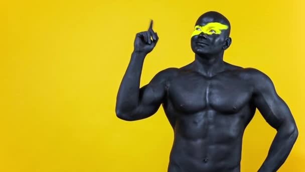 Man have a good idea. Bodybuilder athlete with yellow face art and black body paint. Colorful portrait of the guy with bodyart. Slow motion. — Stock Video