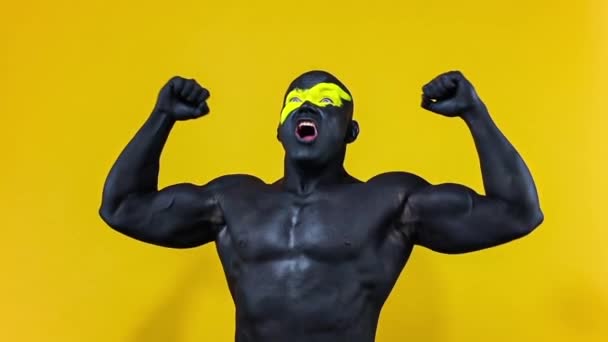 Man sportfan viert teamoverwinning of doelpunt. Bodybuilder atleet met gele kleur op gezicht kunst en zwarte body paint. Kleurrijk portret van de man met bodyart. Langzame beweging. — Stockvideo