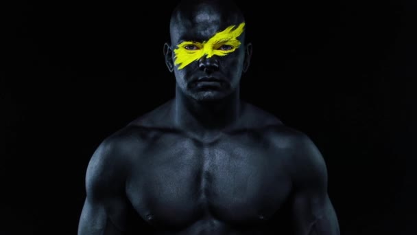 Man sports fan and bodybuilder athlete with yellow color on face art and black body paint. Colorful portrait of the guy with bodyart. Slow motion. — Stock Video