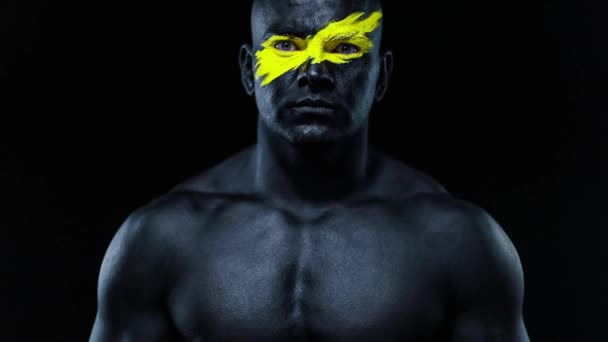 Retrato de close-up do homem fisiculturista atleta com cor amarela na arte facial e pintura corporal preta. Foto colorida do cara com bodyart. Movimento lento . — Vídeo de Stock