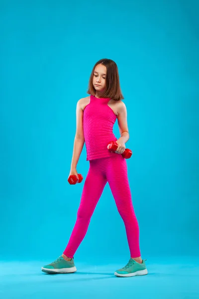 Menina fazendo exercícios de fitness com halteres no fundo azul — Fotografia de Stock