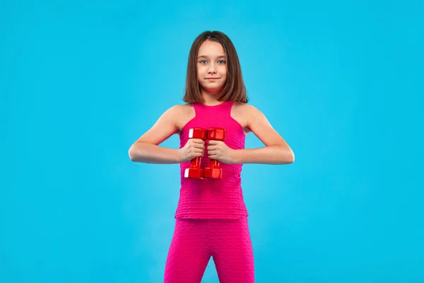 Menina fazendo exercícios de fitness com halteres no fundo azul — Fotografia de Stock