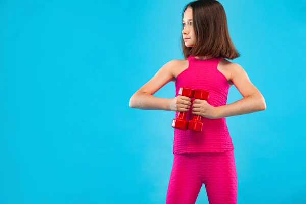 Menina fazendo exercícios de fitness com halteres no fundo azul — Fotografia de Stock