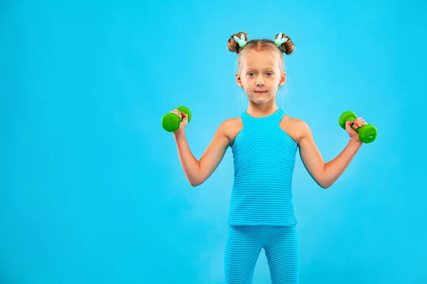 Дитяча дівчинка робить фітнес або вправи для йоги з гантелями ізольовані на синьому фоні — стокове фото