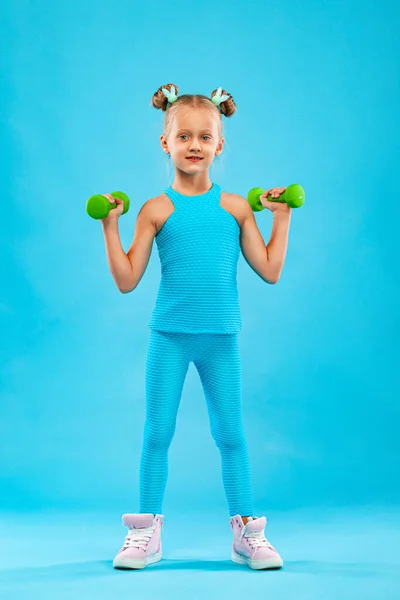 Дитяча дівчинка робить фітнес або вправи для йоги з гантелями ізольовані на синьому фоні — стокове фото