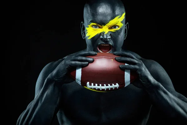 Αμερικανός οπαδός του ποδοσφαίρου με μπάλα σε μαύρο φόντο. Γυμναστική και αθλητικά κίνητρα. Δυνατός και αθλητικός τύπος στο σώμα ζωγραφίζει σαν σούπερ ήρωας.. — Φωτογραφία Αρχείου