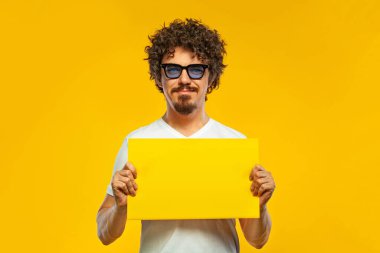 Boş afişi ya da posteri olan bir Mab. Sarı arka planda sakallı, beyaz tişörtlü, sırıtan yakışıklı, mutlu Avrupalı bir adam. Yaşam tarzı kavramı.