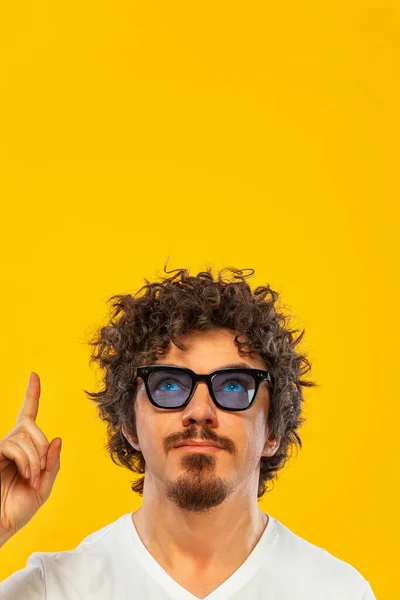 Portrait of happy bearded man with curly hair pointing finger up at copyspace isolated over yellow background. Guy in blue sunglasses pick on great idea. — 图库照片