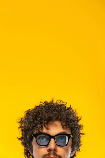 Portrait of happy bearded man with curly hair pointing finger up at copyspace isolated over yellow background. Guy in blue sunglasses pick on great idea. — 图库照片