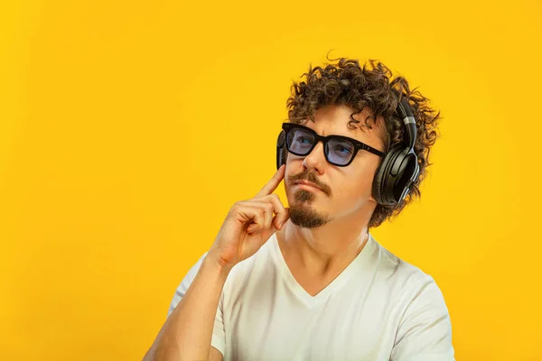 Porträtt av glad skäggig man med lockigt hår pekar finger åt skärmen isolerad över gul bakgrund. Killen i blå solglasögon och hörlurar hacka på bra idé. — Stockfoto