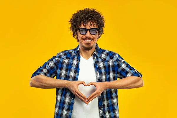 快乐胡子男人的画像，卷曲的头发，用手指表示心脏，黄色背景隔离. — 图库照片