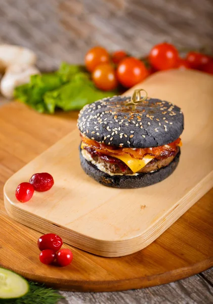 Чорний гамбургер з беконом і соусом на дерев'яній підставці Ліцензійні Стокові Зображення